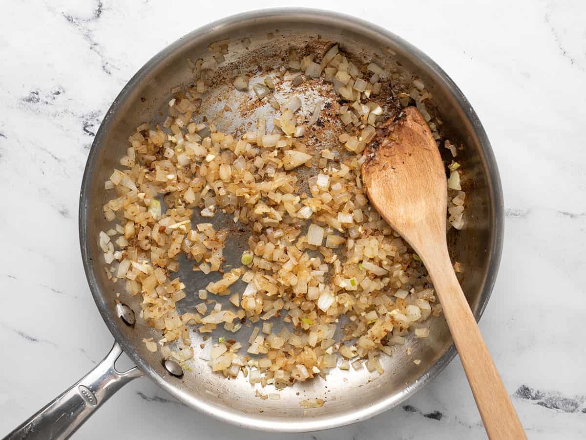 Overhead shot of onions cooking in ground beef fat in silver sauté pan.