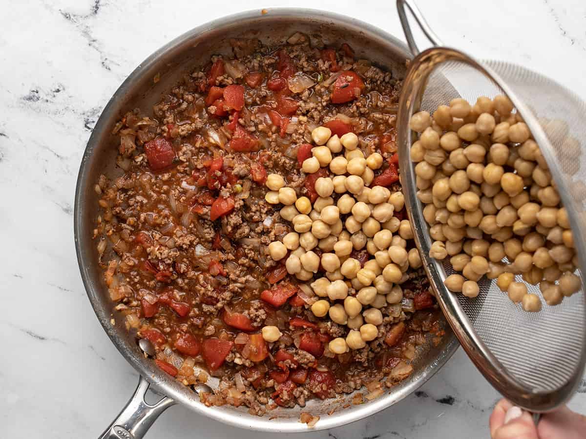 Overhead shot of garbanzo beans added to ground beef mixture in sauté pan.