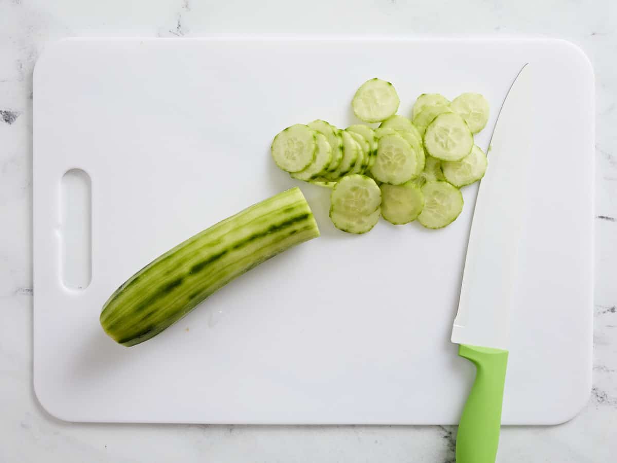 Peeled and sliced cucumber on a cutting board.