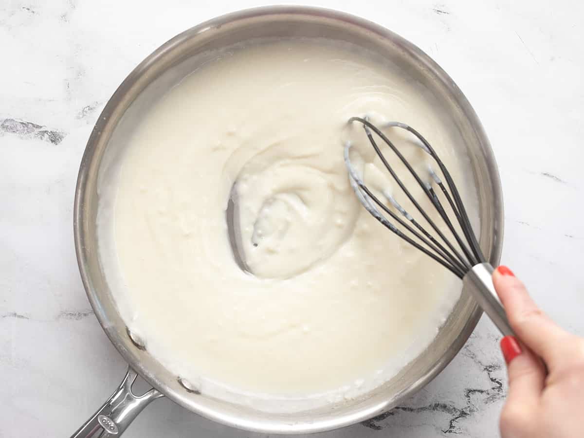 Thickened white sauce in the skillet being whisked.