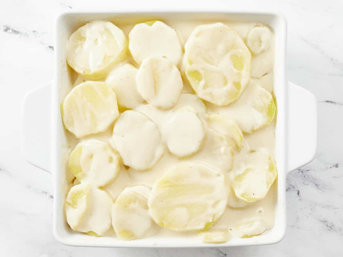Overhead shot of raw scalloped potatoes covered in cream sauce in a white casserole dish.