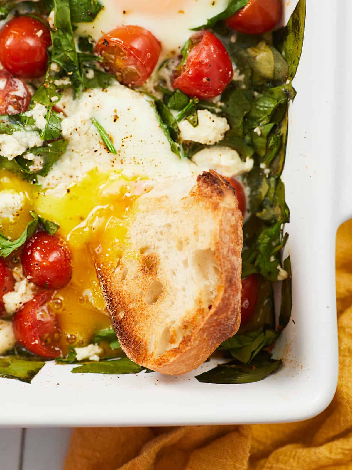 Close up overhead view of bread dipping into a casserole dish full of baked eggs.