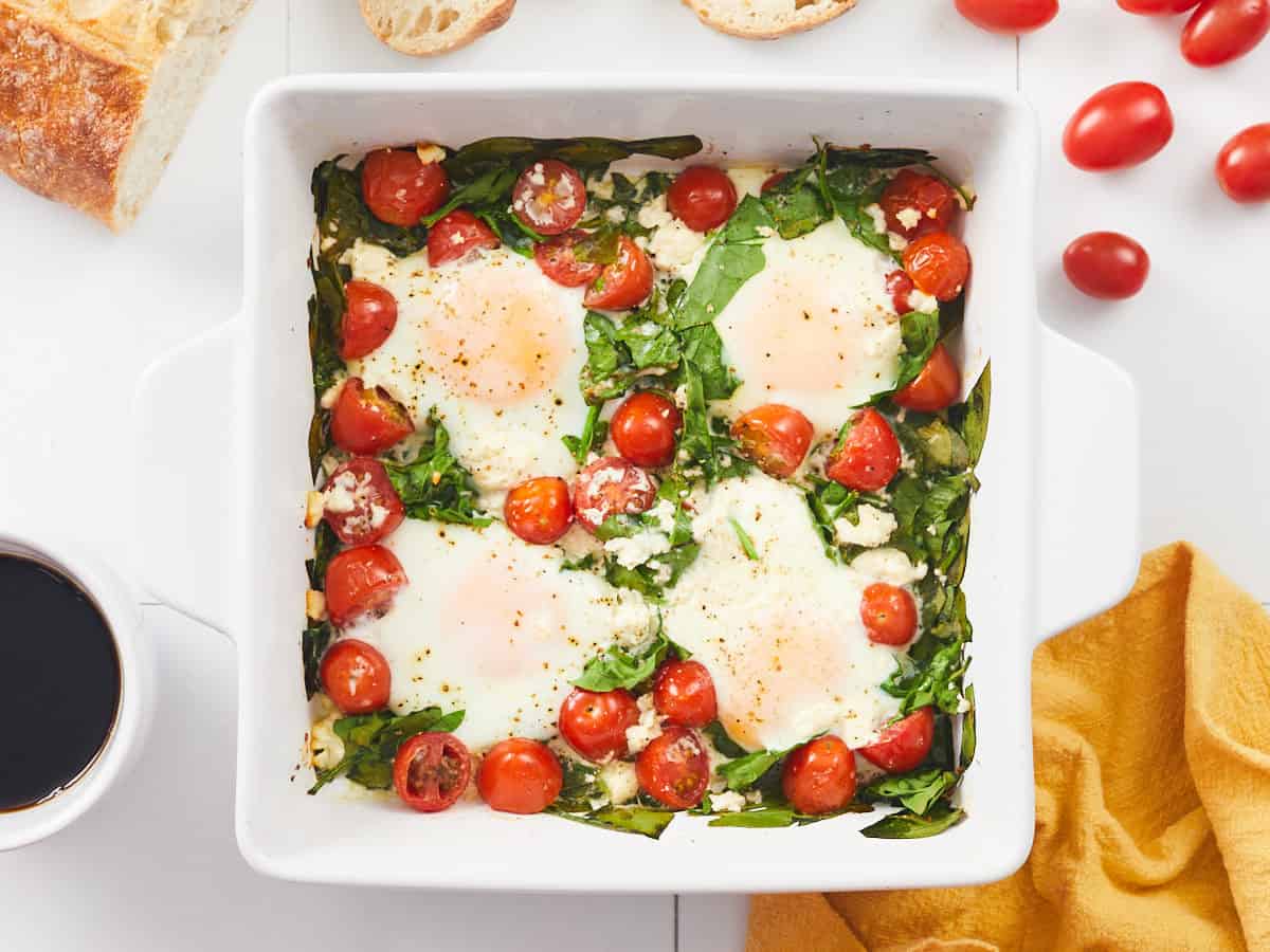 Overhead view of a casserole dish full of baked eggs with spinach and tomatoes.
