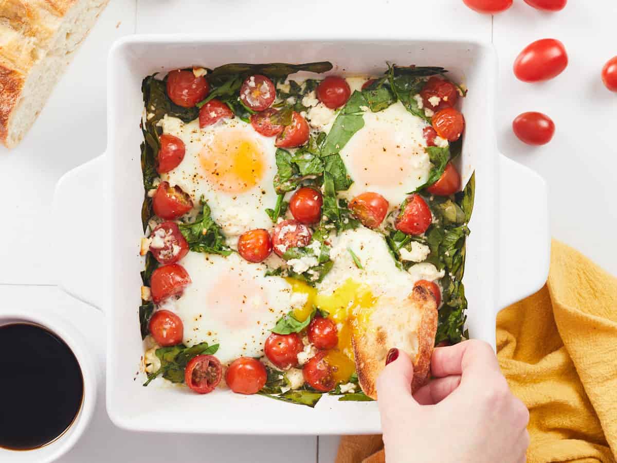 Overhead view of bread being dipped into baked eggs. 