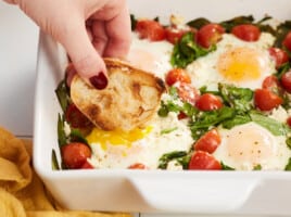 Side view of bread being dipped into a casserole of baked eggs.