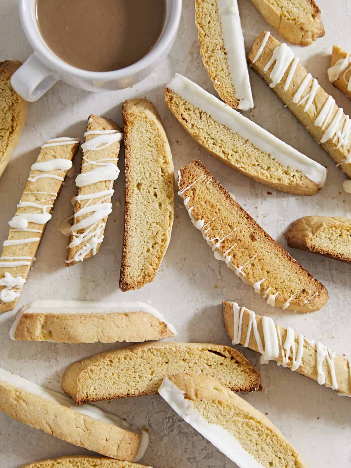 Scattered biscotti on a surface with a cup of coffee.