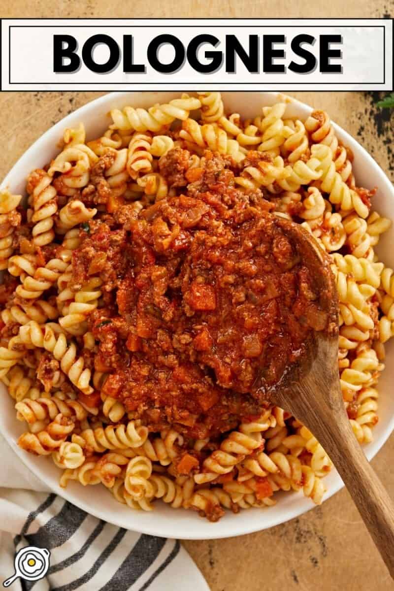 Overhead view of a plate full of pasta with bolognese sauce being spooned over top.