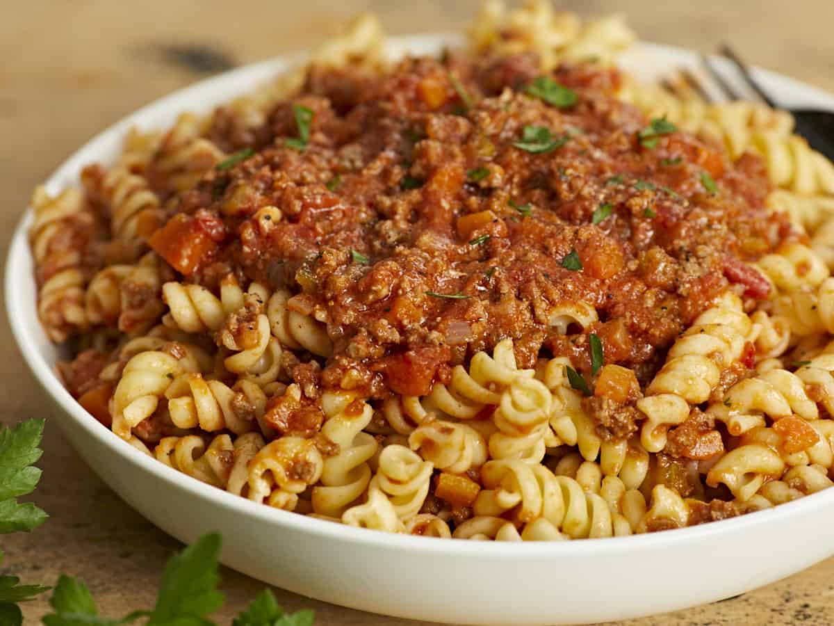 Side shot of bolognese served over rotini in a white bowl.