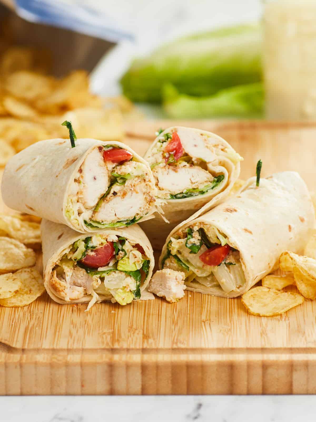 Stacked chicken Caesar wraps on a cutting board with chips in the background.