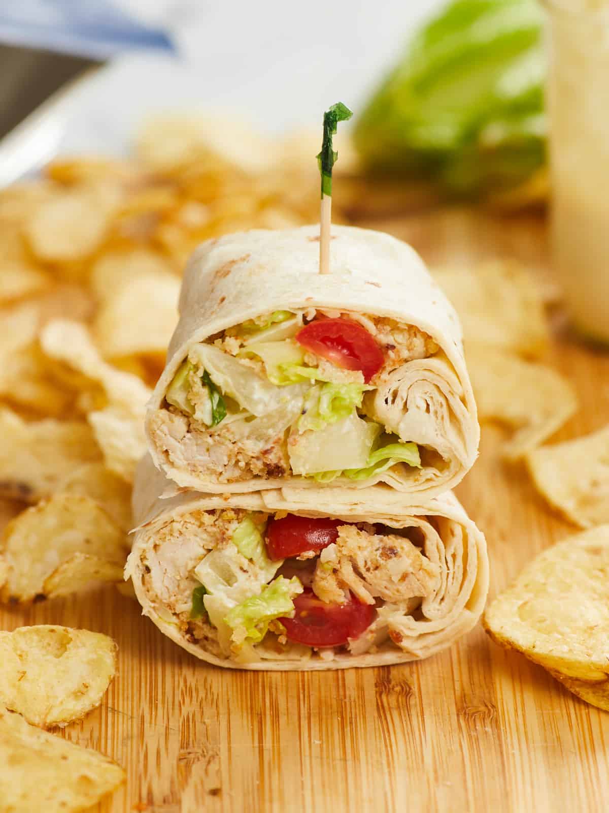 Front view of a chicken Caesar wrap cut in half and stacked on a cutting board.