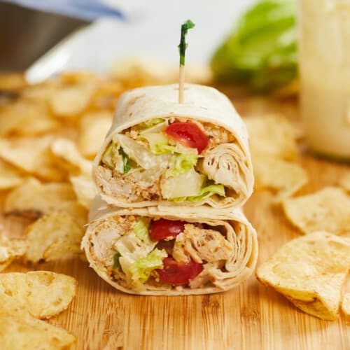 Side view of a chicken Caesar wrap cut in half and stacked on a cutting board.