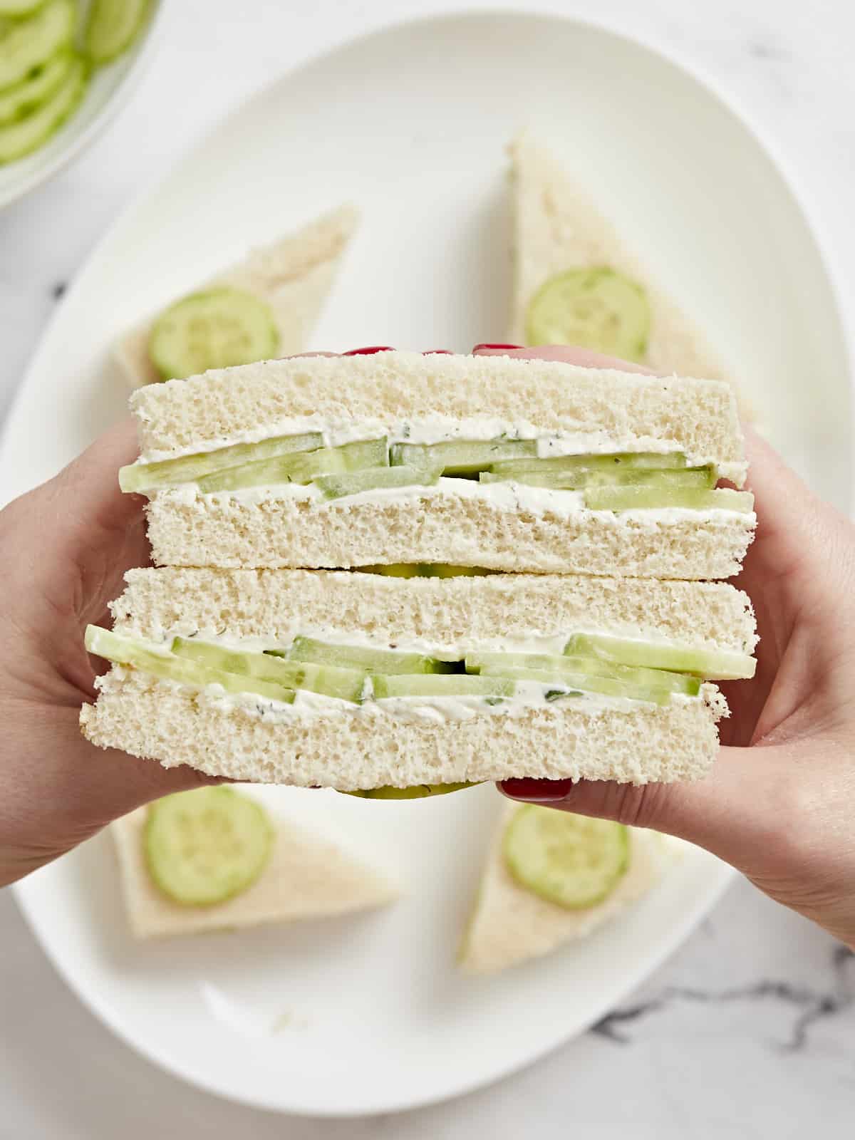 Side view of a hand holding stacks of cucumber sandwiches.