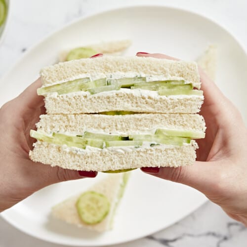 Side view of hands holding a stacked cucumber sandwich.