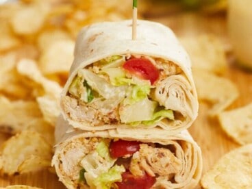 Front view of a chicken Caesar wrap cut in half and stacked on a cutting board.