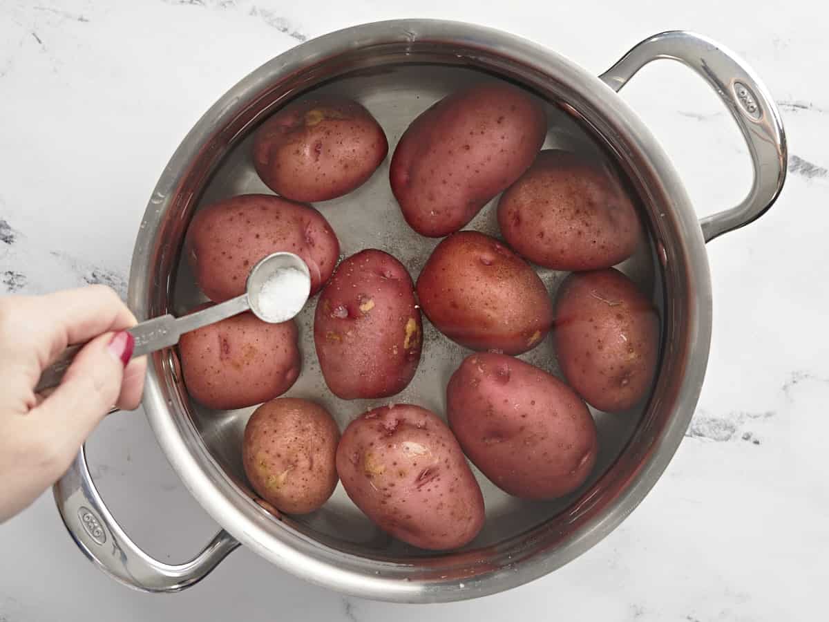 Potatoes in a pot of water with salt being sprinkled over top. 