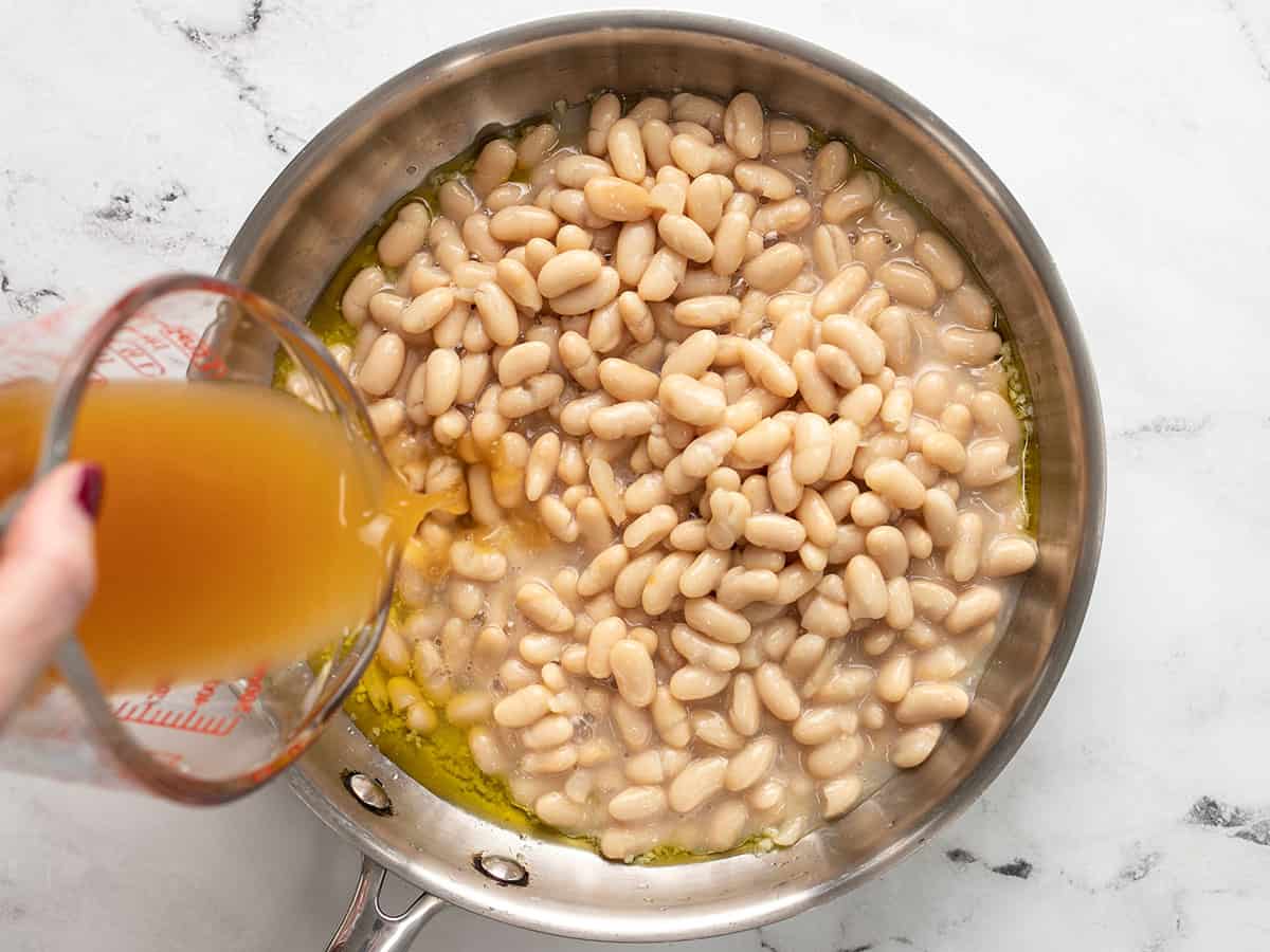 Bean added to the skillet, broth being poured in the side.