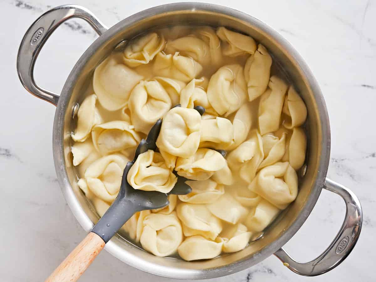 Boiled tortellini in a pot being stirred with a pasta spoon.