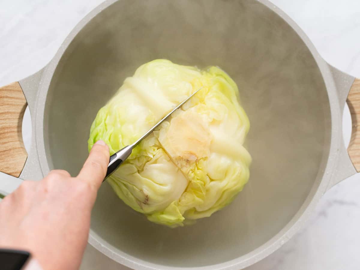 Overhead view of softened outer leaves being removed from the cabbage with a pairing knife.