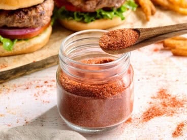 Side view of homemade burger seasoning in a jar with a spoon.