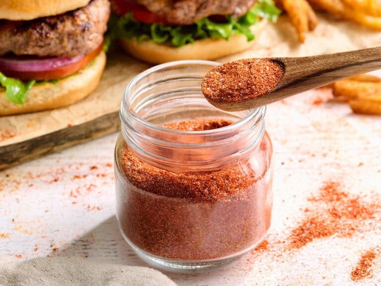 Side view of homemade burger seasoning in a jar with a spoon.