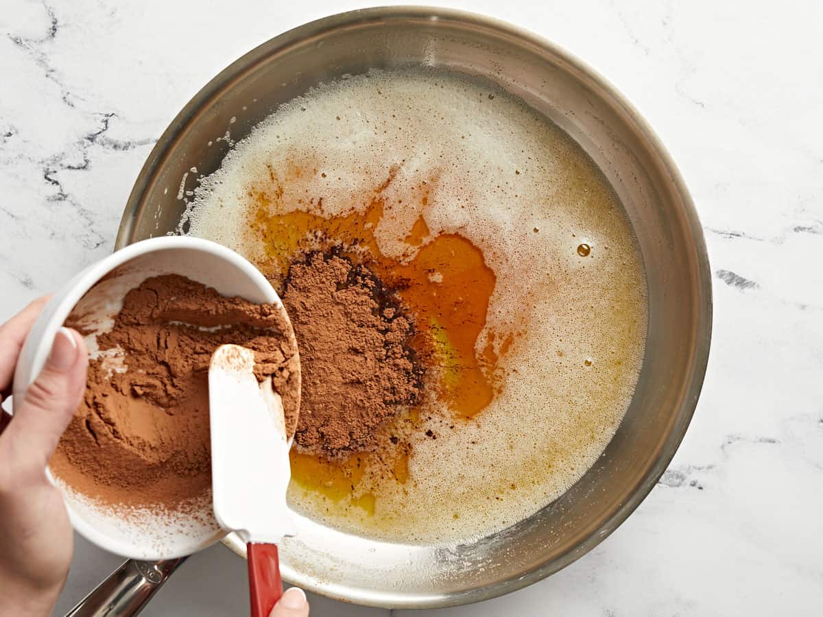 Cocoa powder being added to browned butter in a skillet.