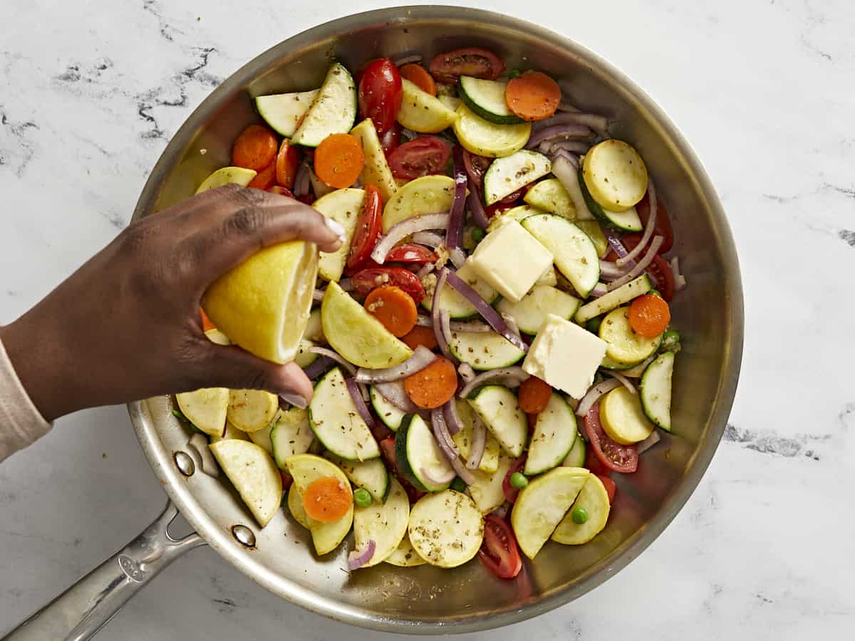Lemon being squeezed over the vegetables in the skillet.