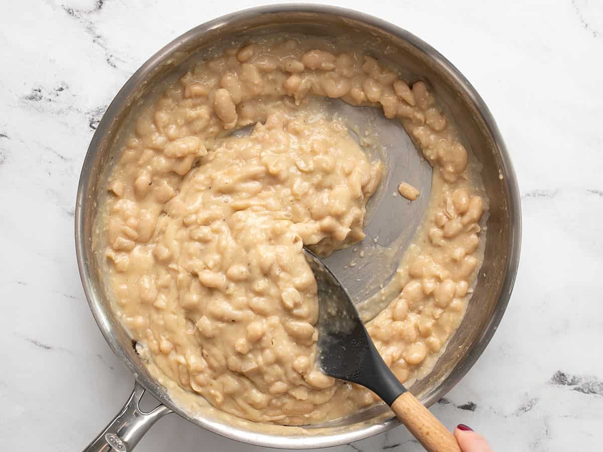 Thickened beans being stirred with a spoon.