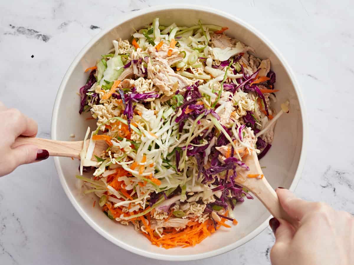 Salad being tossed with two wooden utensils.