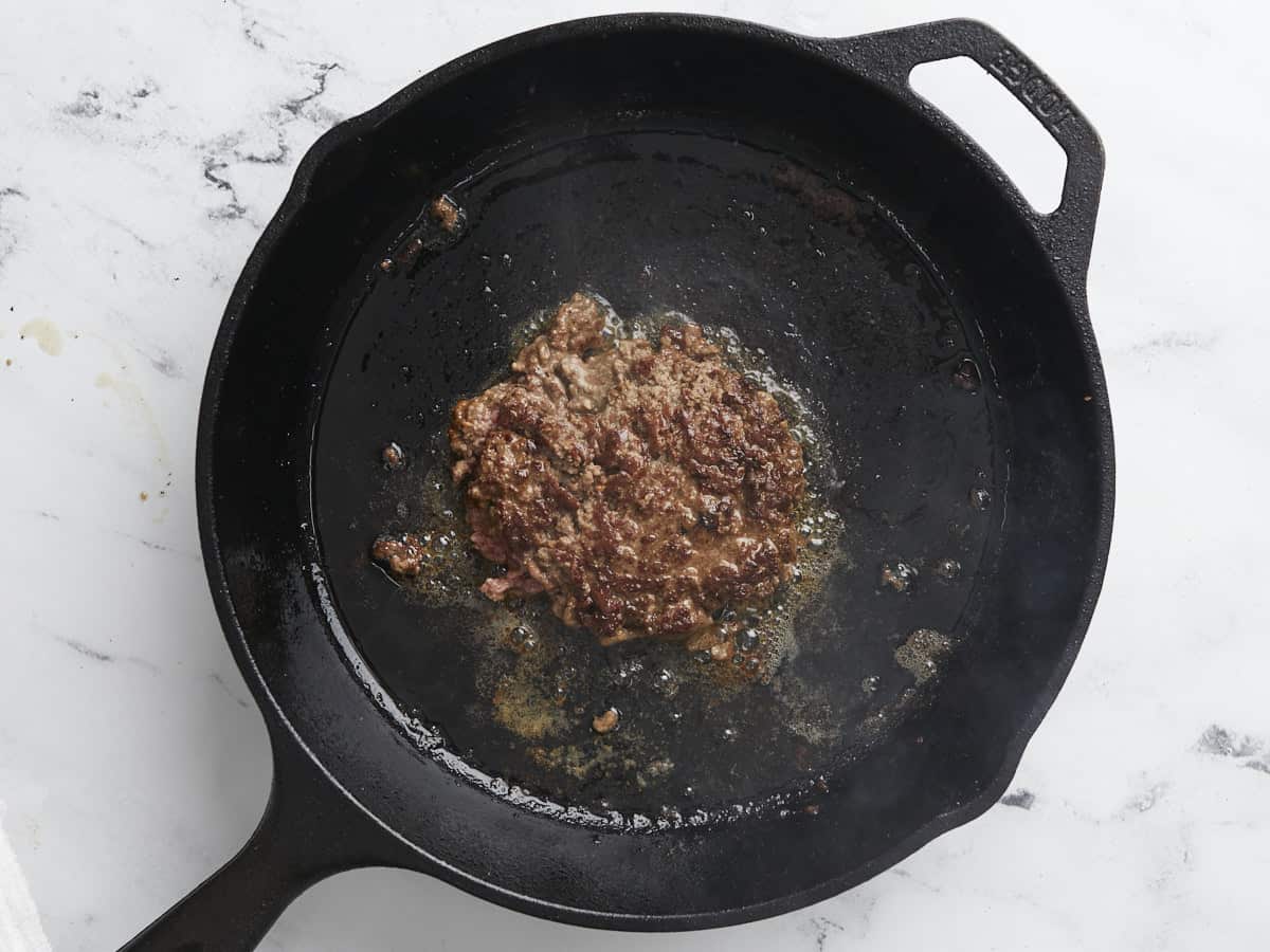 Overhead shot of cooked Smashed Burger patty in a black cast iron pan.