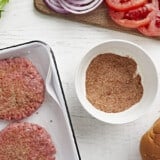 burger seasoning being sprinkled over hamburger patties.