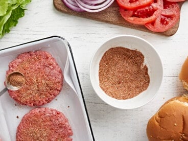 burger seasoning being sprinkled over hamburger patties.