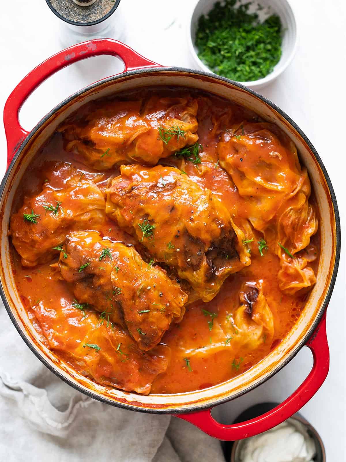 Cabbage rolls in a large stock pot covered with tomato sauce and garnished with fresh dill.