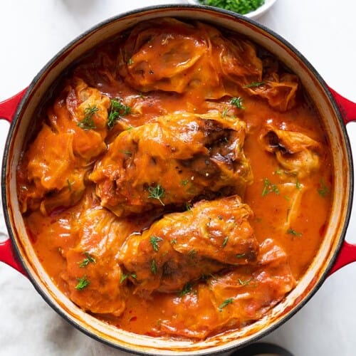 overhead view of cabbage rolls in a stock pot with tomato sauce poured on top and garnished with fresh dill