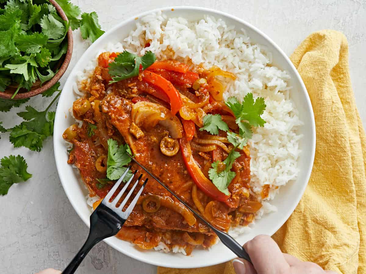 Chuletas Guisadas on a plate with rice being cut with knife and fork.