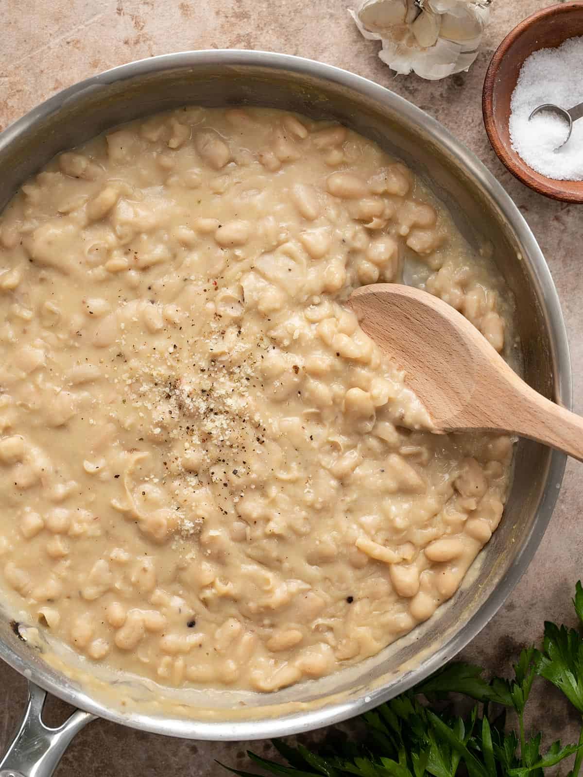 Overhead view of a skillet full of Parmesan beans with a wooden spoon.