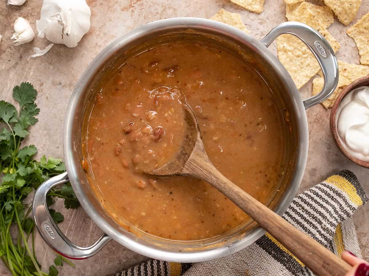 Overhead view of a pot full of pinto bean soup with a wooden spoon.