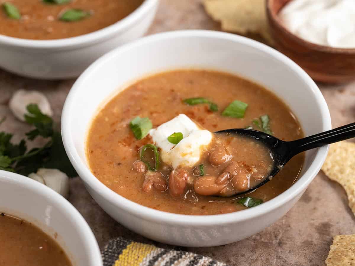 Side view of a bowl of pinto bean soup with sour cream and a spoon lifting the soup.