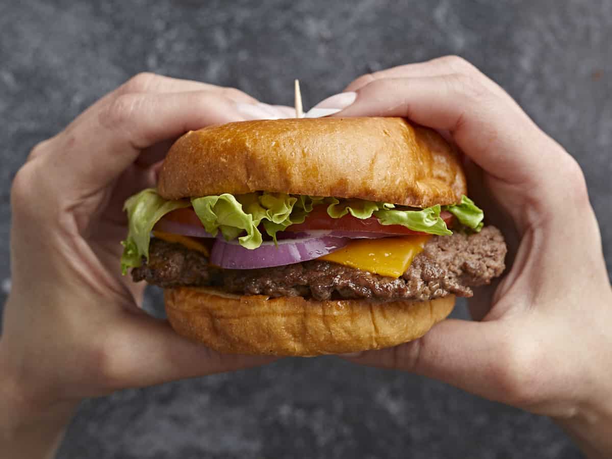 Side view of Smash Burger being held by two hands.