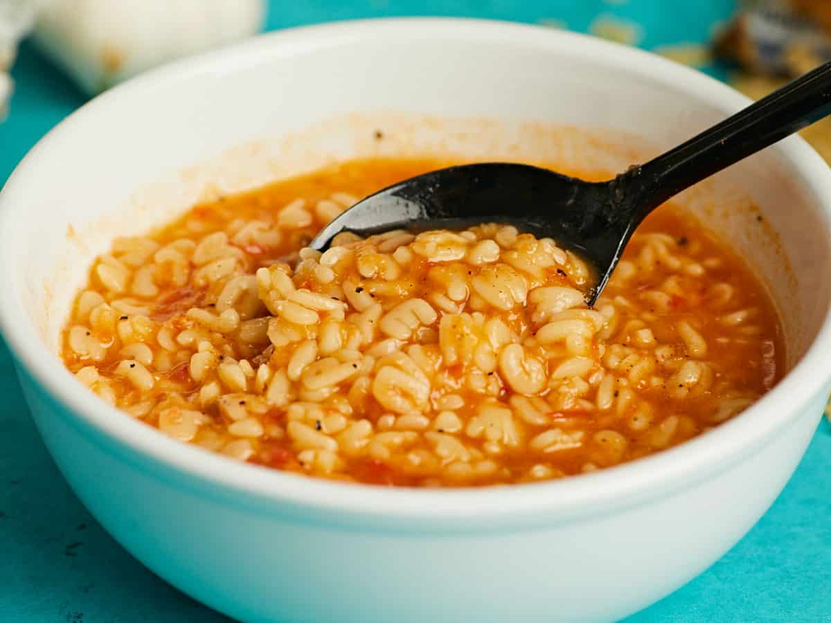 Side view of a spoon dipping into a bowl of sopa de letras. 