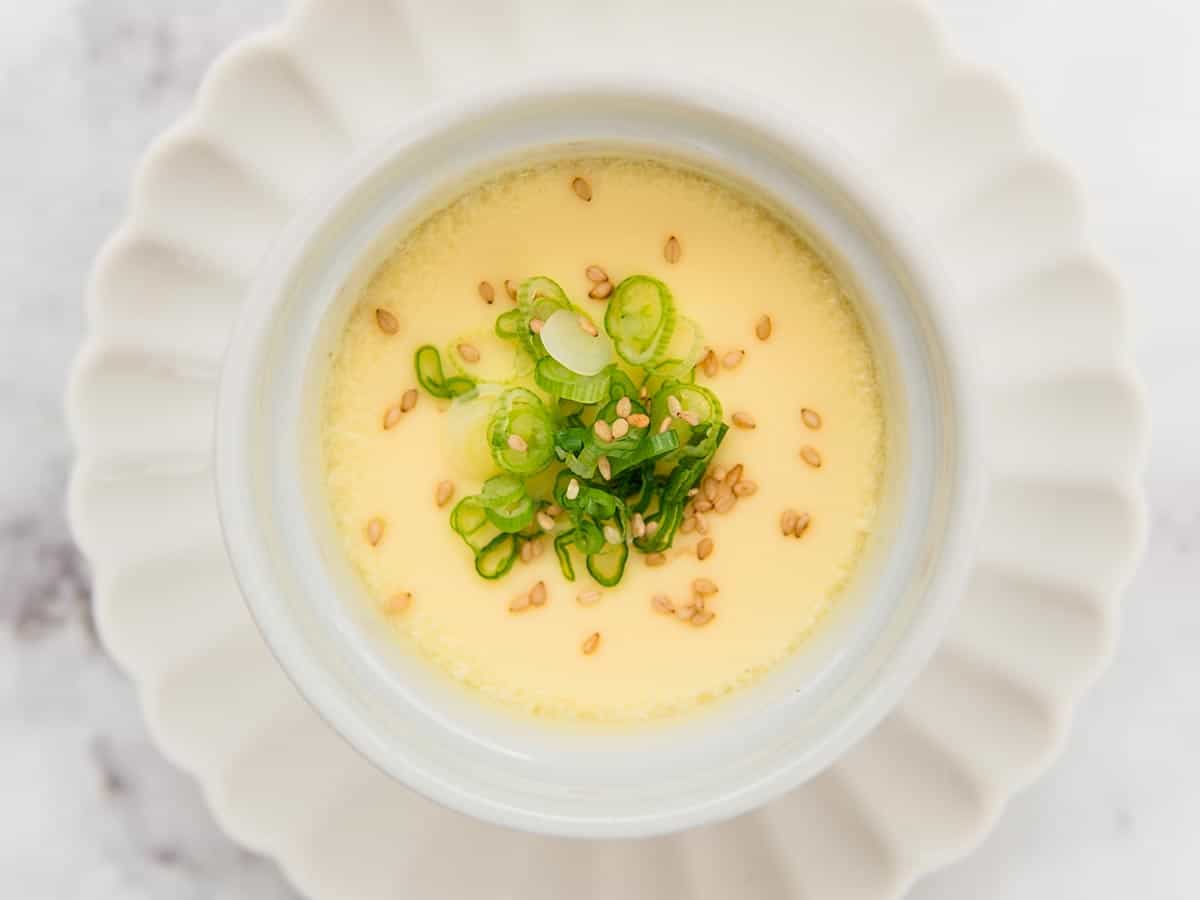 Steamed eggs in a white ramekin garnished with finely sliced green onions and a sprinkle of sesame.
