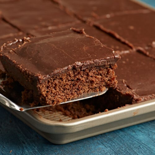 A slice of chocolate cake being lifted out of the sheet pan.