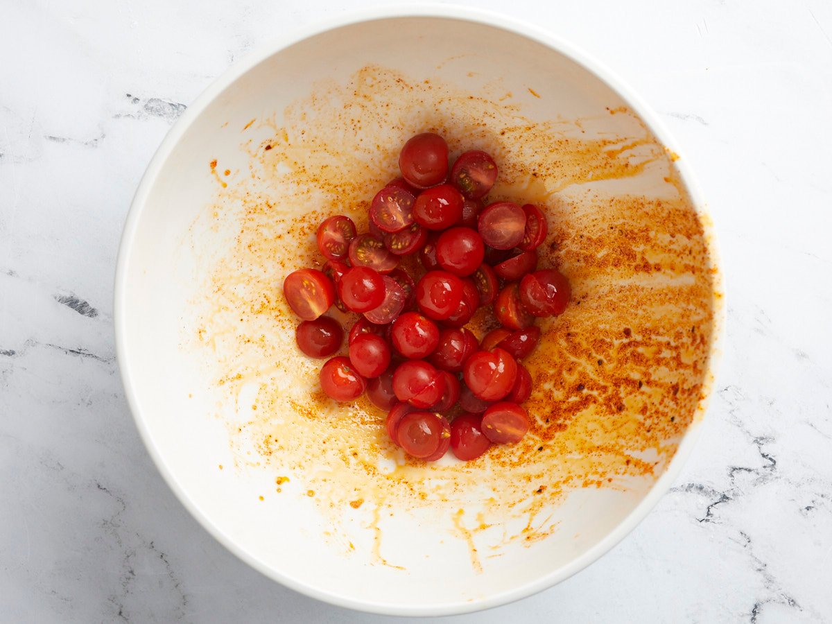 Overhead shot of tomatoes being dressed in a white bowl.