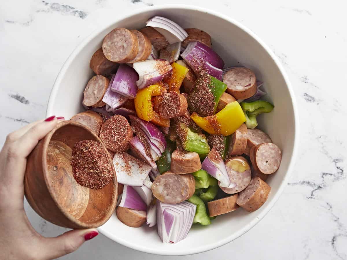 Sausage and vegetables in a bowl with seasoning being sprinkled over top.