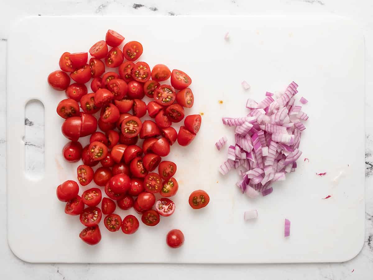 Sliced grape tomatoes and diced red onion on a cutting board.