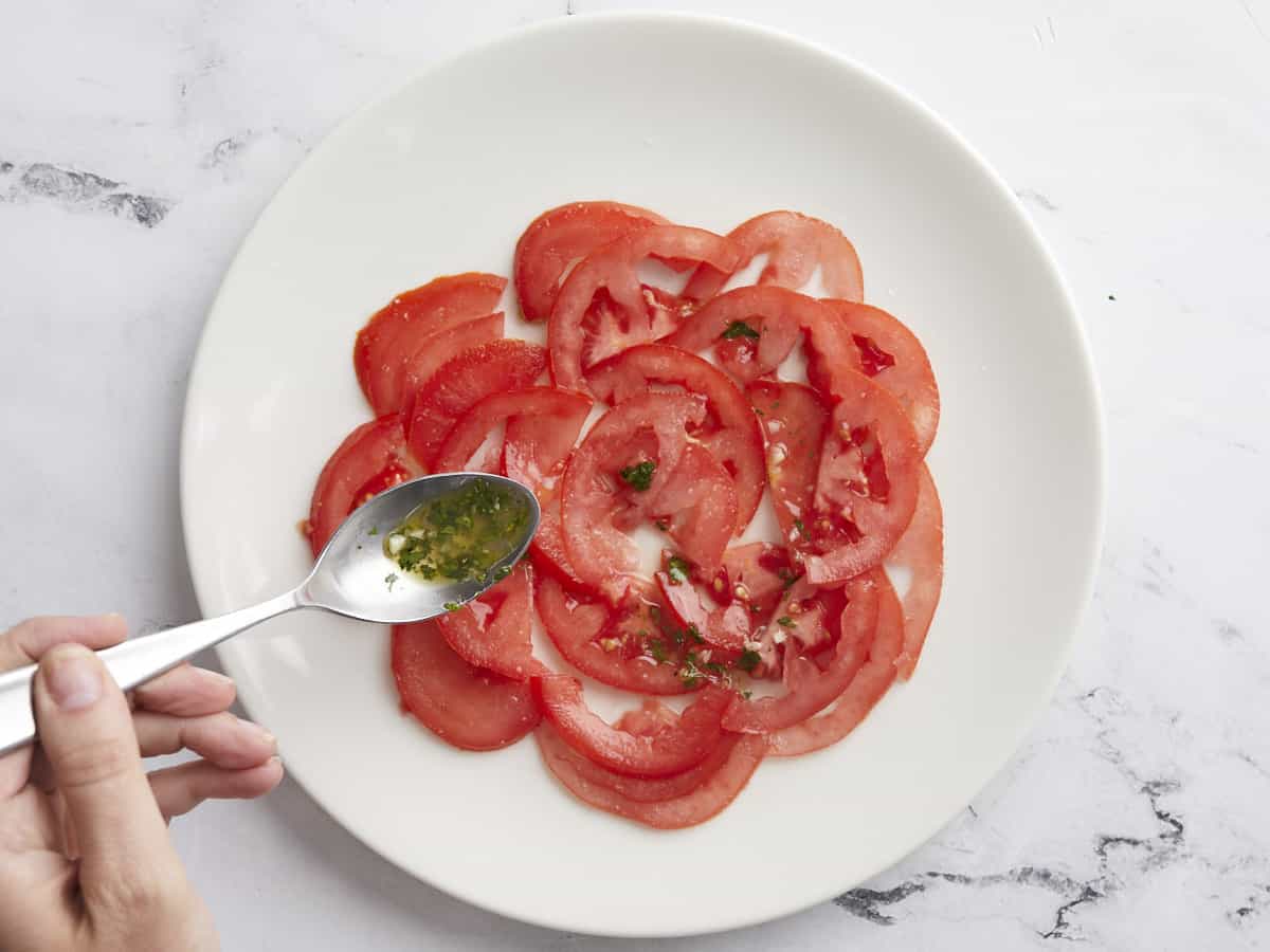 Overhead shot of tomatoes on a white plate with dressing being spooned over them.