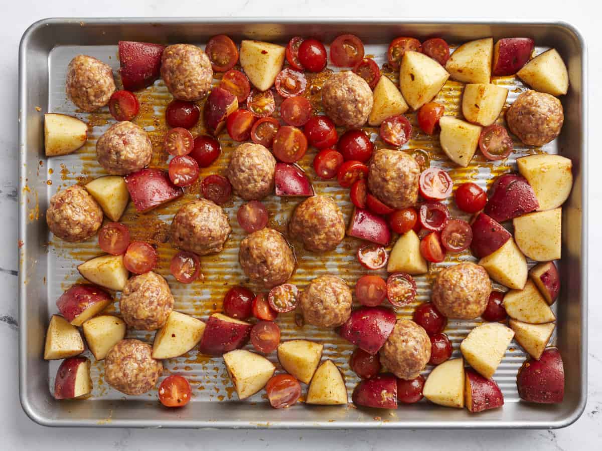 Overhead shot of meatballs, potatoes, and tomatoes in sheet pan.