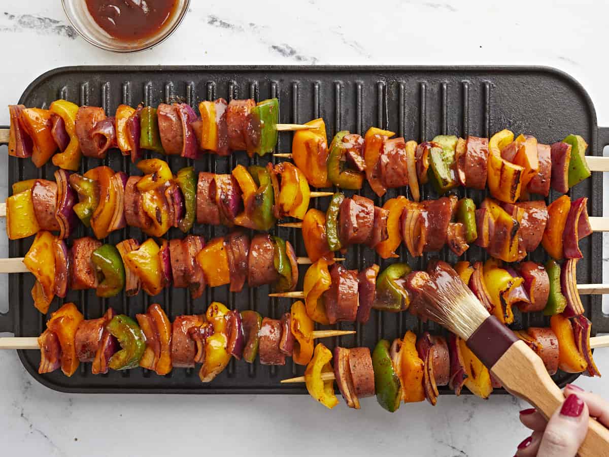 Sausage kebabs on the grill pan with BBQ sauce being brushed over top.