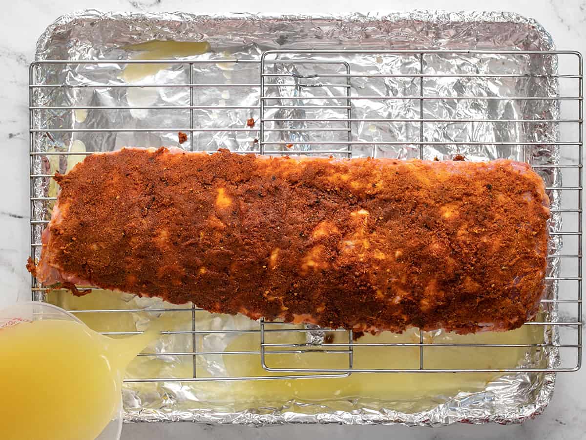 Adding broth to a sheet pan with ribs on a rack.