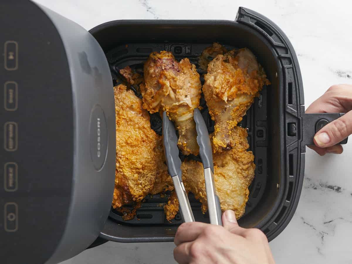 Fotografía cenital de pinzas volteando pollo frito en una freidora de aire.