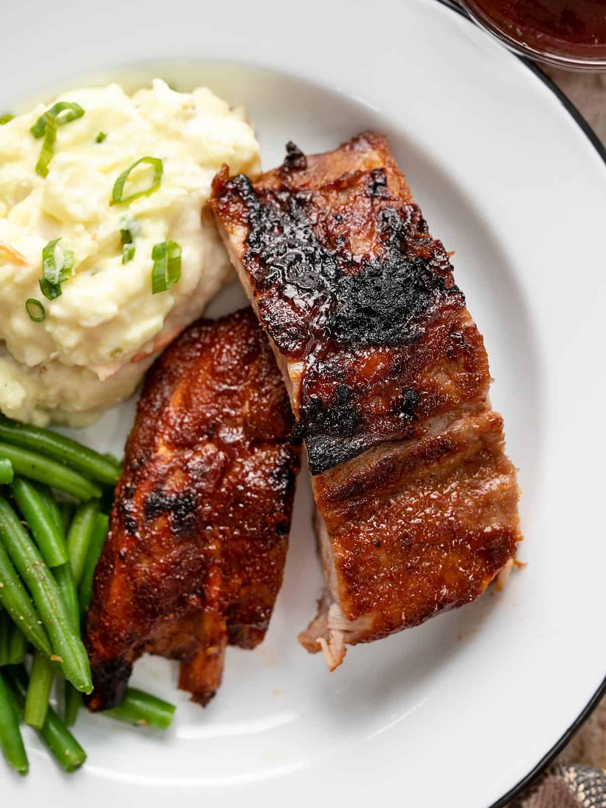 Cut ribs on a white plate with mashed potatoes and green beans.